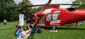 Des enfants sont assis devant un hélicoptère de sauvetage et posent des questions à un pilote de la Rega