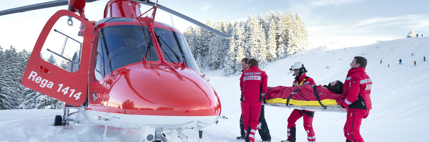 Die Rega-Crew trägt mit Hilfe des Pistenpatrouilleurs einen verletzten Wintersportler zum Helikopter.