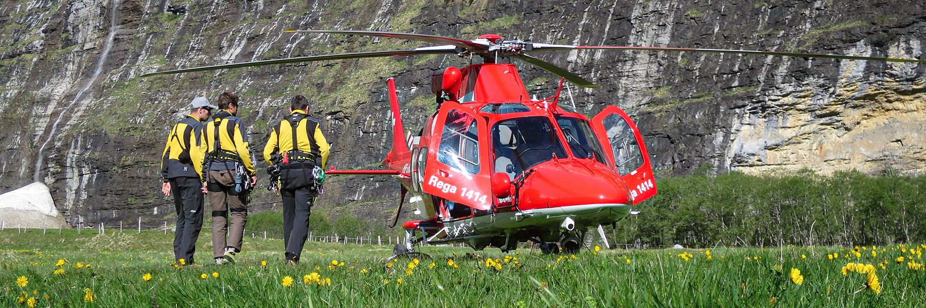 Three SAC mountain rescuers stand next to an AgustaWestland rescue helicopter