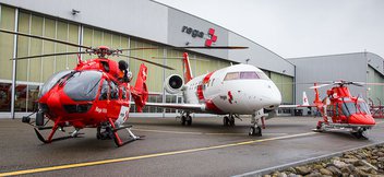 Deux hélicoptères de sauvetage et un avion-ambulance devant la porte d’un hangar