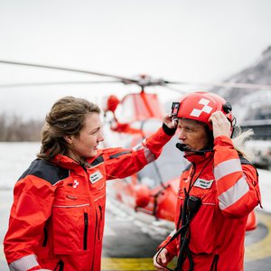 Two people in front of a Rega helicopter