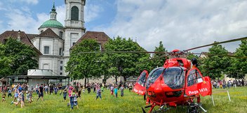 Des enfants courent vers un hélicoptère de la Rega pour l’observer de plus près